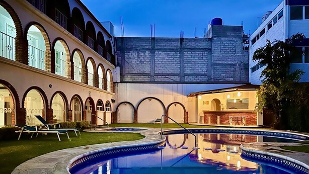 A pool area with a circular pool, lounge chairs, and a building with arched windows and a brick facade. - Hotel el Romano Ixtapan de la Sal  (Ixtapan de la Sal)