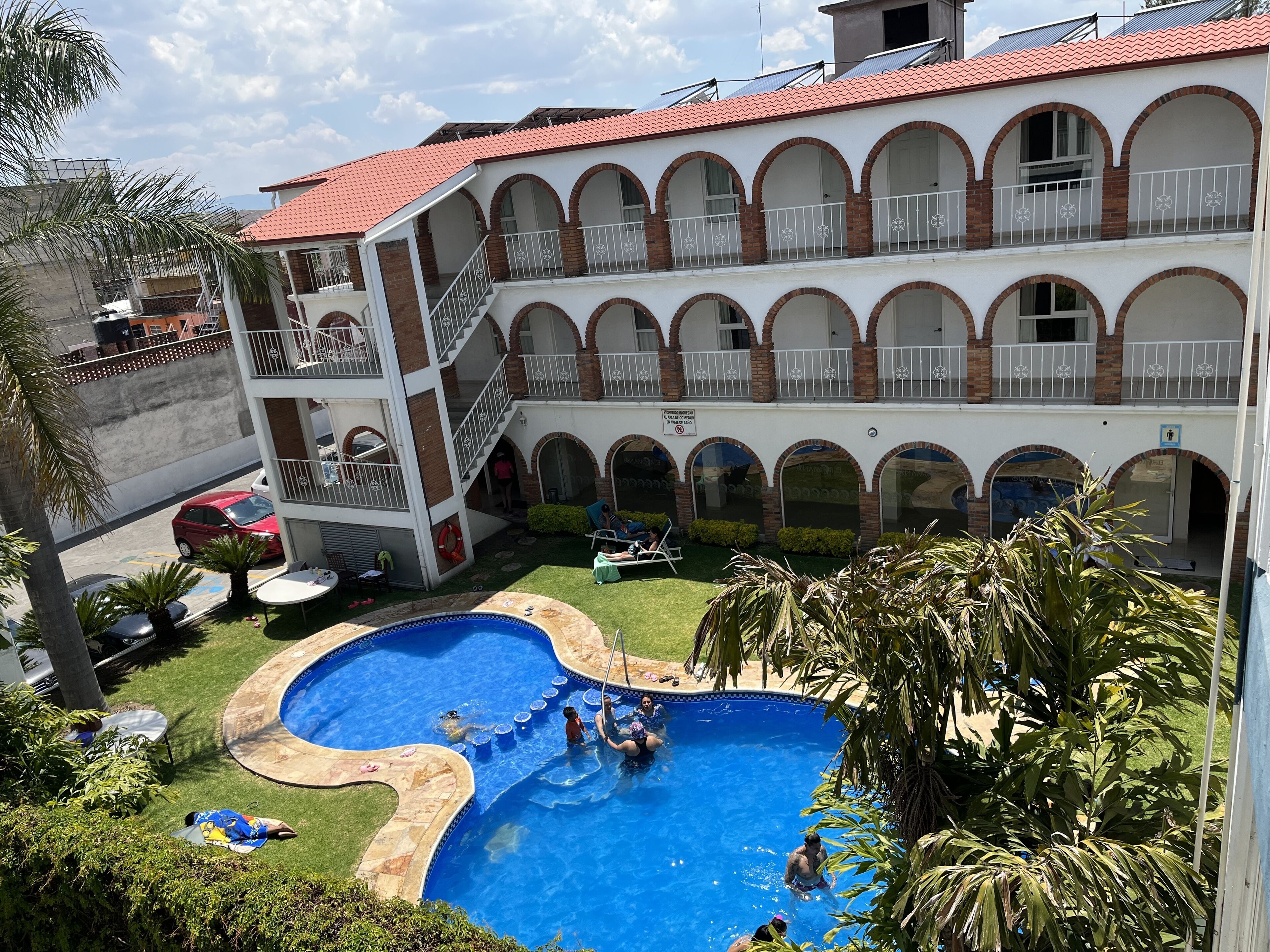 A multi-story building with a swimming pool, outdoor seating, and a covered patio area.