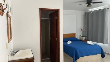 Habitación de hotel con cama, baño con lavamanos, ventilador de techo y ventana con cortinas.