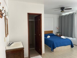 Habitación de hotel con cama, baño con lavamanos, ventilador de techo y ventana con cortinas.