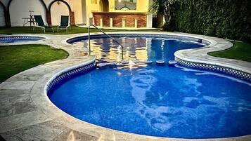 Una piscina con borde de azulejos, un área de barbacoa de ladrillo y una zona de estar cubierta con sillas.