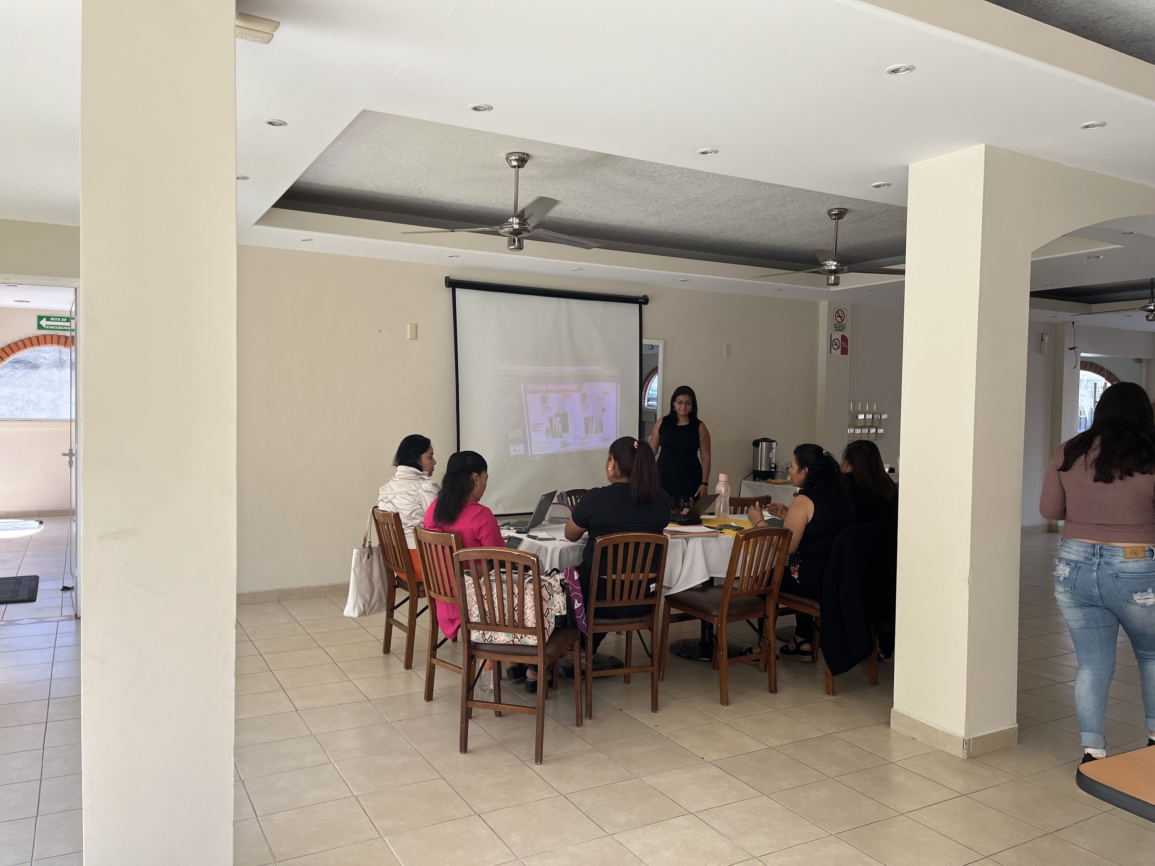 A conference room with a projector screen, wooden chairs, and a table with laptops and documents.