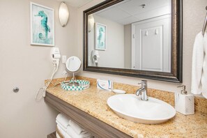 Une salle de bain dotée d’un comptoir en granit, d’un lavabo blanc, d’un grand miroir et d’une œuvre d’art représentant un hippocampe, encadrée et accrochée au mur.