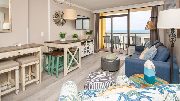 A modern living room with a sofa, ottoman, and a dining area with a table and chairs. - Oceanfront | Amazing Views & Sunrises (Myrtle Beach)