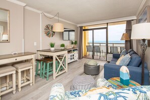 A modern living room with a sofa, ottoman, and a dining area with a table and chairs. - Oceanfront | Amazing Views & Sunrises (Myrtle Beach)