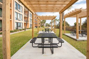 Un espace extérieur abrité avec des tables de pique-nique, une allée en béton et un bâtiment doté de balcons en arrière-plan.