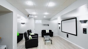 Una sala de cine en casa moderna con un televisor de pantalla plana grande, asientos cómodos y un proyector instalado en el techo.