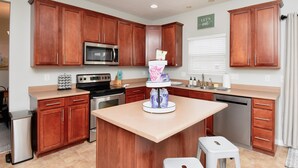 Una cocina moderna con armarios de madera, una isla central, electrodomésticos de acero inoxidable y un letrero que dice 'Let's eat'.