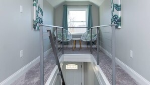 Un escalier avec une rampe en verre, deux chaises blanches et une fenêtre avec des rideaux.