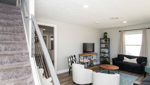 Un salon moderne avec un escalier, un téléviseur à écran plat, un canapé noir et une table basse.