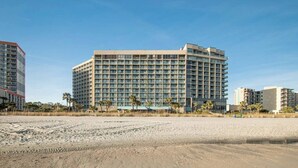 Ein Strandhotel mit einem großen Gebäude, Sandstrand und Palmen.