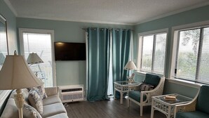 Ein Wohnzimmer mit einer Couch, zwei Sesseln, einem Couchtisch, einem Fernseher und einem Fenster mit Vorhängen.