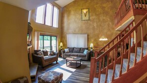 A spacious living room with a large window, a wooden staircase, and a cozy seating area. - Roomy Beautiful Golf/Ski Condo (Clymer)