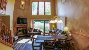 A spacious living room with a fireplace, a television, a dining area with a table and chairs, and a large window offering a view of the outdoors. - Roomy Beautiful Golf/Ski Condo (Clymer)