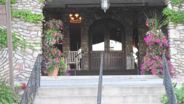A stone building with a wooden staircase leading to a door. There are potted plants with pink flowers on either side of the entrance. - Roomy Beautiful Golf/Ski Condo (Clymer)