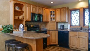 A kitchen with wooden cabinets, a microwave, a stove, a dishwasher, and a bar area with stools. - Roomy Beautiful Golf/Ski Condo (Clymer)