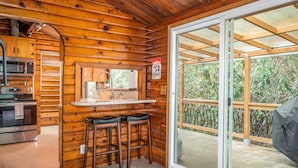 Interno di una baita in legno con cucina, sgabelli da bar e una porta scorrevole in vetro che dà su una terrazza.