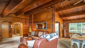 Interno di una baita di legno con un divano in pelle, un tavolo da pranzo in legno e un albero di Natale.