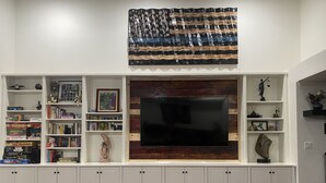 A living room with a TV mounted on a wooden wall, surrounded by shelves with books and decorative items.