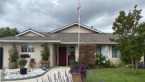A two-story house with a red door, a front yard with various plants, and a flagpole with an American flag.