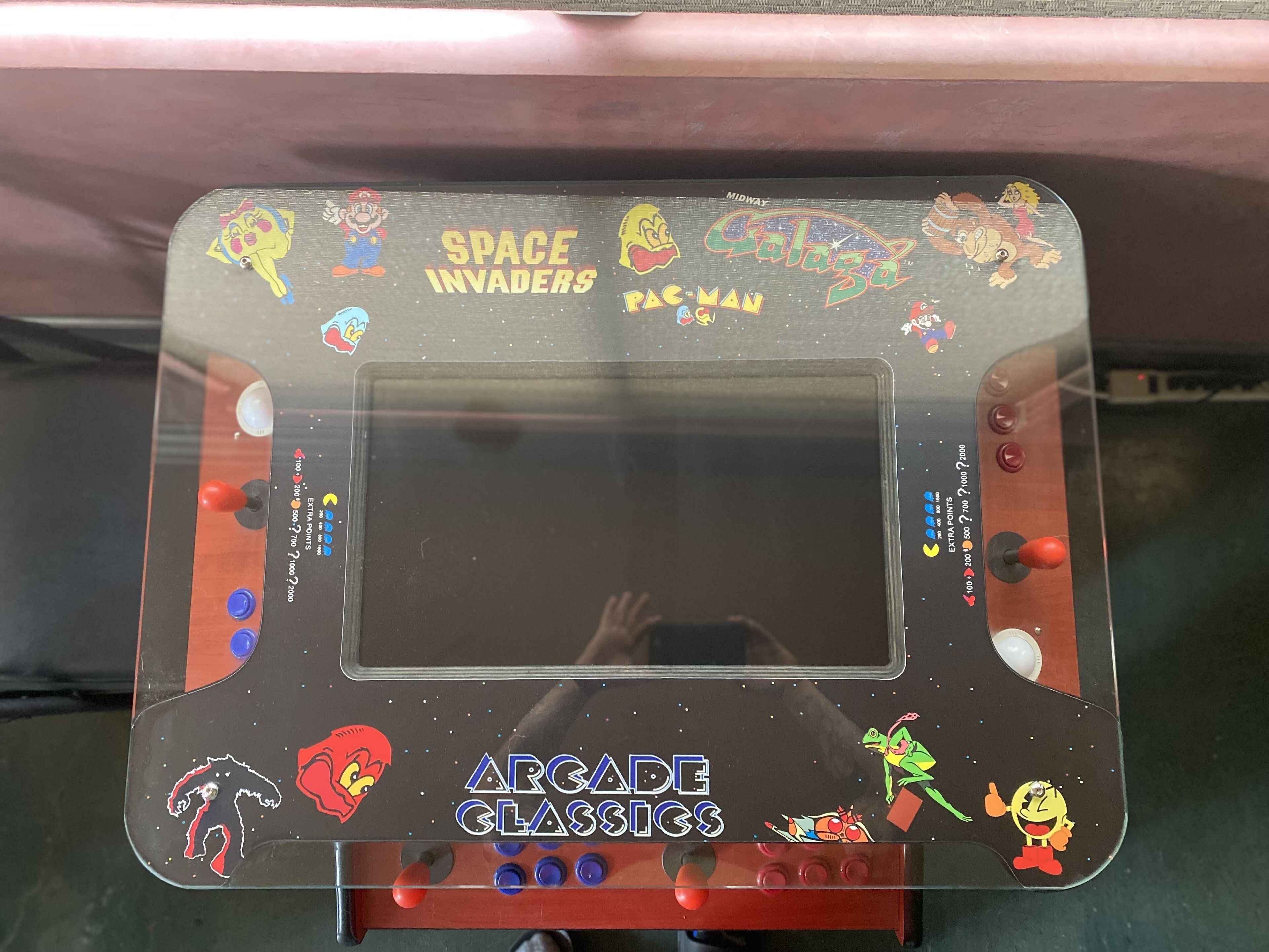 Ein Automatengehäuse im Retro-Stil mit Grafiken zu Space Invaders und Pac-Man, inklusive Joystick-Steuerung und Punktestand-Anzeige.