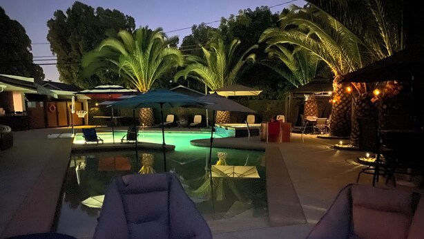 A pool area with lounge chairs and umbrellas, surrounded by palm trees and a stone building.