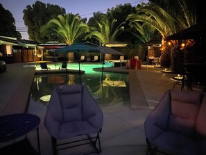 A pool area with lounge chairs and umbrellas, surrounded by palm trees and a stone building. - Family Retreat near Disney, Knotts, Beaches, Aquarium, Gondala, Entertainment.  (Long Beach)