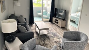 A living room with a sofa, a coffee table, a TV, and a ceiling fan. - Coastal Retreat - 2BR CONDO (Rehoboth Beach)