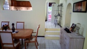 A dining area with a wooden table and chairs, a small cabinet with decorative items, and a staircase leading to an outdoor area. - Caye Manje Holiday Lodge (Gros Islet)