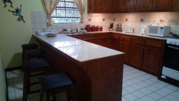 A kitchen with wooden cabinets, a white countertop, a sink, a microwave, and a stove. - Caye Manje Holiday Lodge (Gros Islet)