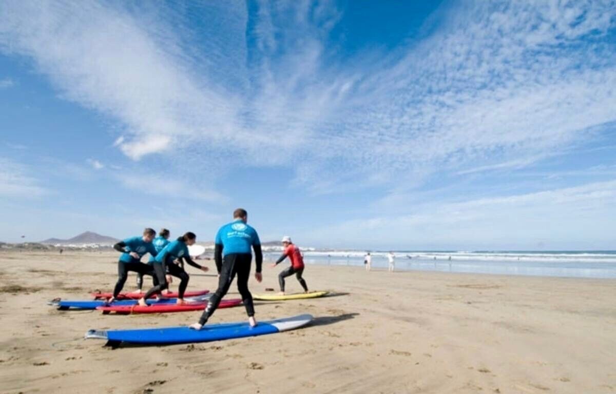 Ranta, jossa ihmiset surffaavat, kirkas taivas ja kaukainen vuori.