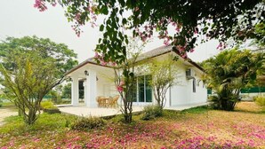 A white building with a covered patio, surrounded by greenery and pink flowers. - Salithyna villa (Vientiane)
