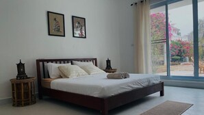 A bedroom with a large bed, two nightstands, a window with a view of flowers, and two framed pictures on the wall. - Salithyna villa (Vientiane)
