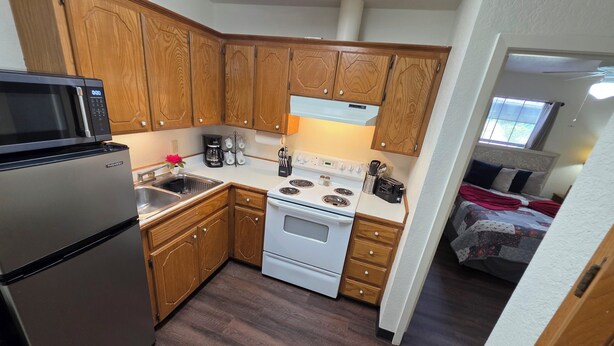 Cocina compacta con gabinetes de madera, un refrigerador de acero inoxidable, una estufa blanca y un microondas.