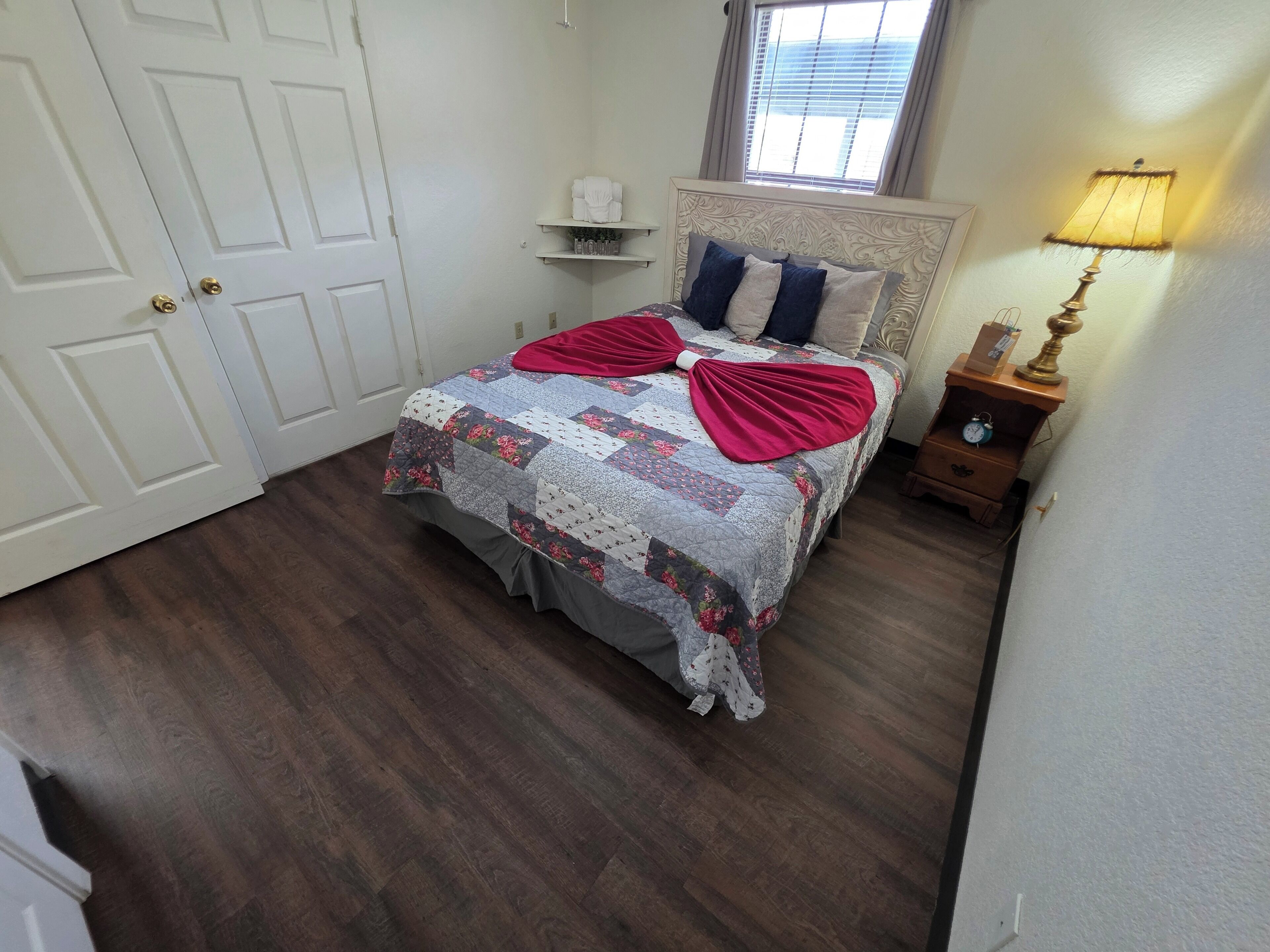 A bedroom with a bed, a nightstand, a lamp, a window, and a door.
