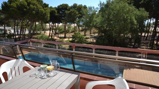 Un espace aménagé au bord de la piscine, avec une table et des chaises, offrant une vue sur la piscine et une zone boisée.