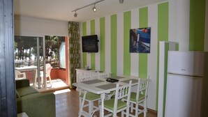Une petite pièce, bien éclairée, avec une table et des chaises, un téléviseur fixé au mur et un réfrigérateur.