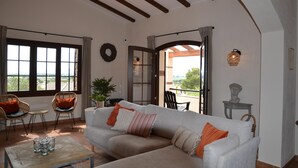 Ein geräumiges Wohnzimmer mit einer großen Couch, zwei Sesseln, einem Couchtisch und Blick durch ein großes Fenster.