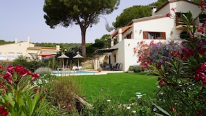 Eine Villa mit Swimmingpool, einem Garten mit unterschiedlichen Pflanzen und einem großen Baum.