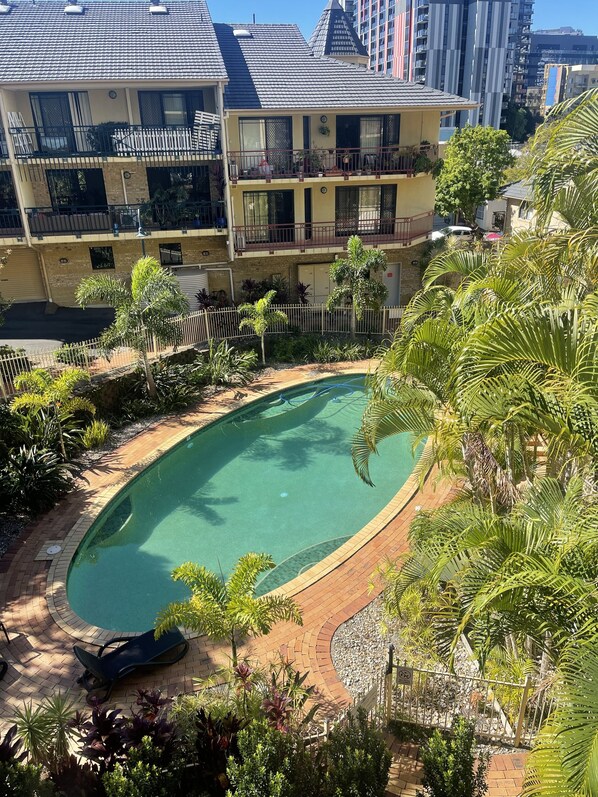 Edificio residencial con piscina rodeada de abundante vegetación y un patio cercado.