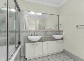 Un baño con dos lavamanos, un espejo grande y zona de ducha.