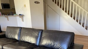 A black leather sectional sofa in a modern living room with a wooden floor, a kitchen in the background, and a staircase with white railings. - Nearby Showgrounds and James St and King Williams Precints (Fortitude Valley)