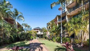 A hotel courtyard with a paved walkway, palm trees, and a building with balconies. - Nearby Showgrounds and James St and King Williams Precints (Fortitude Valley)