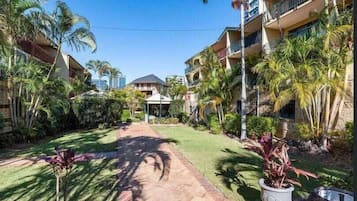 Stroll through the serene courtyard, surrounded by lush greenery and palm trees, to a cozy covered seating area.