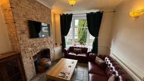 Ein gemütliches Wohnzimmer mit Kamin aus Backsteinen, Ledersofas, einem Holztisch und einem flachbildfernseher an der Wand.