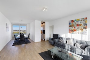A modern living room with a glass coffee table, grey sofa, and a dining area with a table and chairs.