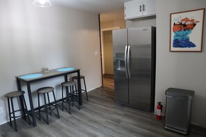 Uma cozinha moderna com geladeira de aço inoxidável, uma pequena mesa de jantar com banquetas e um extintor de incêndio.
