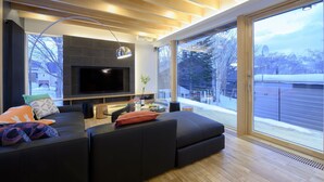 Ein modernes Wohnzimmer mit einem großen Flachbildfernseher, dunklen Sofas und einem Glastisch.