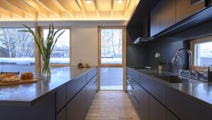 Eine moderne Küche mit Holzbalkendecke, großen Fenstern und einer zentralen Kochinsel.