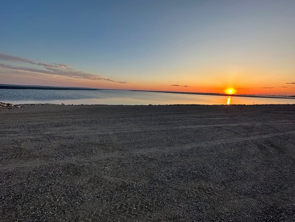 A sunset over a calm body of water with a pebbly shore. - Devils Lake’s Hidden Gem (Devils Lake)